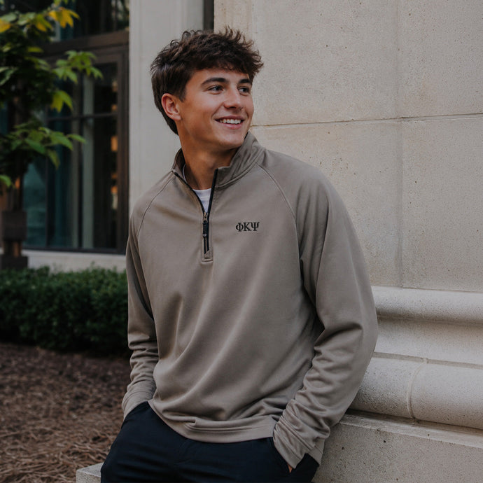 College-aged man wearing the Mushroom Cutter & Buck Adapt quarter-zip with black embroidered Phi Kappa Psi Greek letters outdoors on campus.