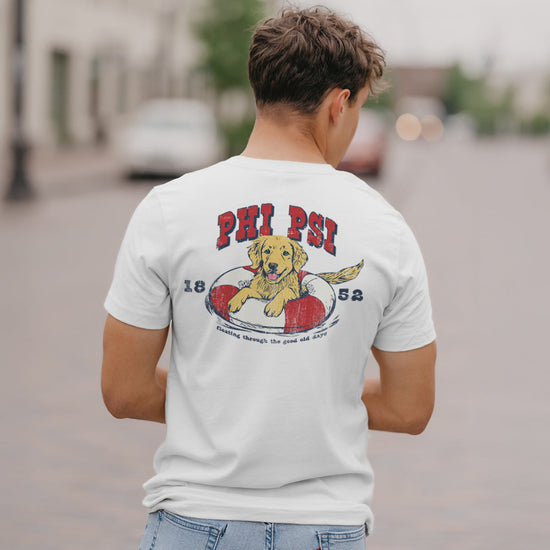 Phi Kappa Psi  fraternity member in a limited edition  white short sleeve tee  featuring a golden retriever puppy playing in an pool floatie  with the fraternity name written above and the founding year.