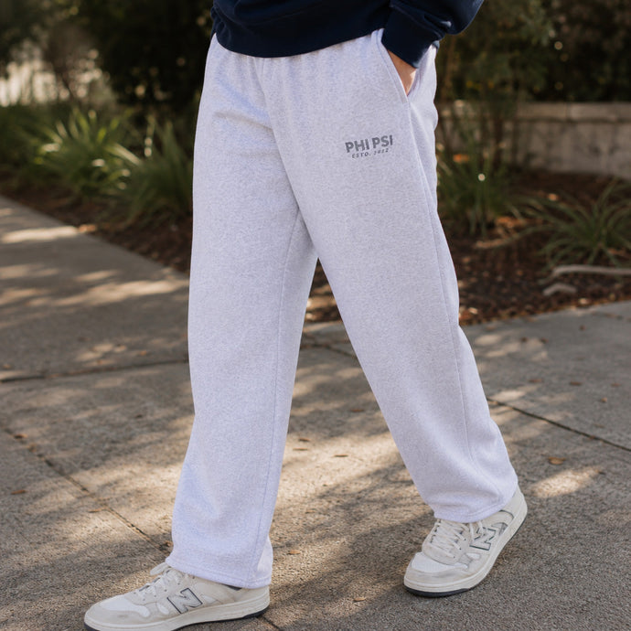 Close-up lifestyle photo of a college-aged male wearing ash gray classic sweatpants with a relaxed straight-leg fit, paired with a navy sweatshirt and white sneakers outdoors.