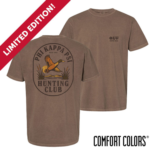Brown garment-dyed short-sleeve tee featuring a vintage-inspired graphic: a weathered oval frames a mallard in mid-flight with burnt orange and mossy green-tipped wings above rippling water and cattails; distressed Phi Kappa Psi arcs overhead and Phi Psi letters bold and rugged on the front.